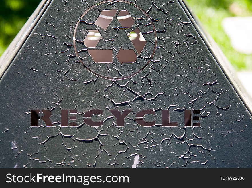Recycle word and symbol cut out of metal with outdoor stret scene in background. Recycle word and symbol cut out of metal with outdoor stret scene in background
