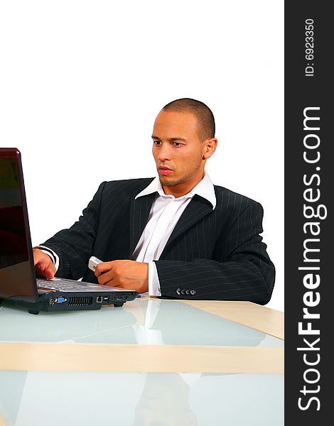 A young businessman sitting by desk at office working on the laptop with cellphone in his hand. Isolated over pure white. A young businessman sitting by desk at office working on the laptop with cellphone in his hand. Isolated over pure white.