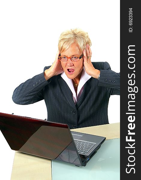 A businesswoman in her sixties in front of a laptop shocked with her hands on her head. Isolated over white. A businesswoman in her sixties in front of a laptop shocked with her hands on her head. Isolated over white.