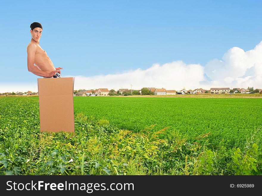 Young man in carton at level field with village on horizon. Young man in carton at level field with village on horizon