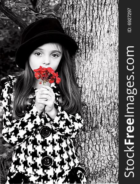 Little girl standing by a tree wearing a coat and hat holding a flower. Little girl standing by a tree wearing a coat and hat holding a flower.