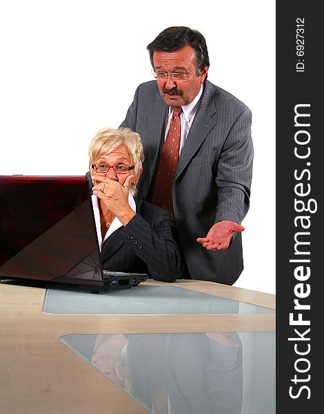 A business woman and a man in front of a laptop on a desk. The man explains something to the woman. She is shocked. Isolated over white. A business woman and a man in front of a laptop on a desk. The man explains something to the woman. She is shocked. Isolated over white.