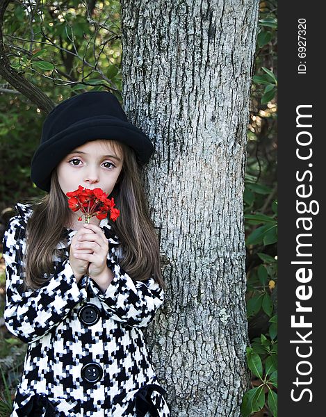 Little girl standing by a tree wearing a coat and hat holding a flower. Little girl standing by a tree wearing a coat and hat holding a flower.