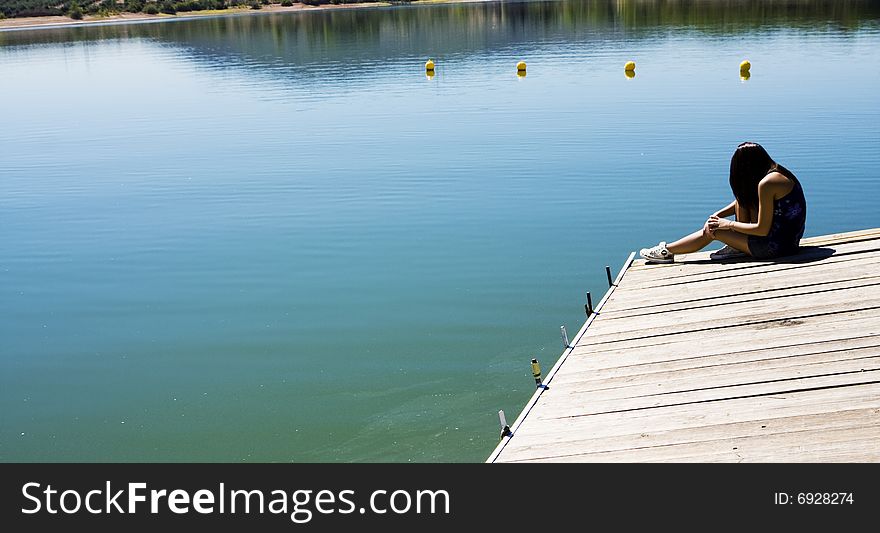 Young woman sitting in a pier in a lake. Young woman sitting in a pier in a lake.