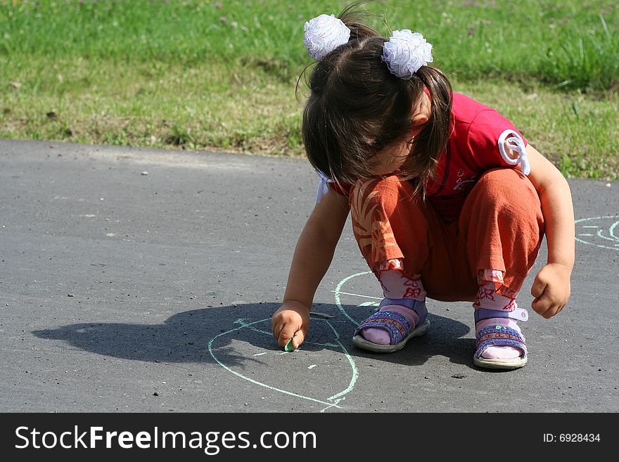 Little girl is drawing on asphalt