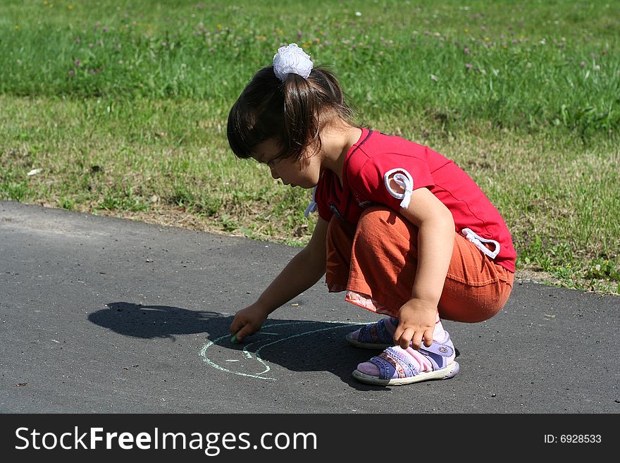Little girl is drawing on asphalt