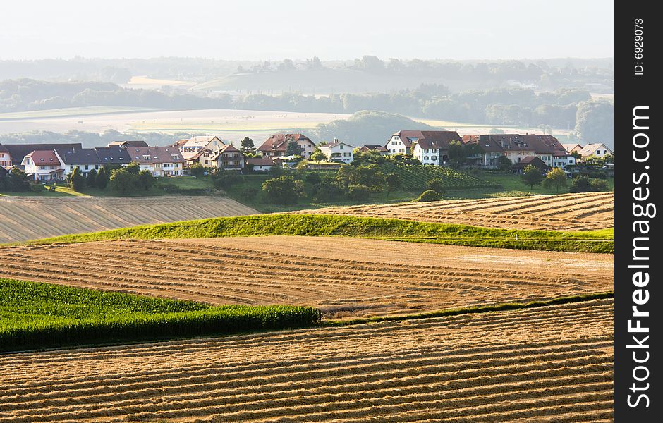 Rural landscape with fields being harvested and village in the background