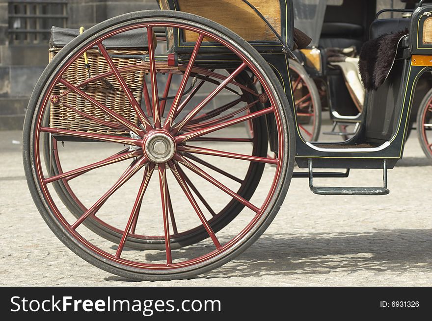 Painted cart wheel on cobblestones with part of a carriage