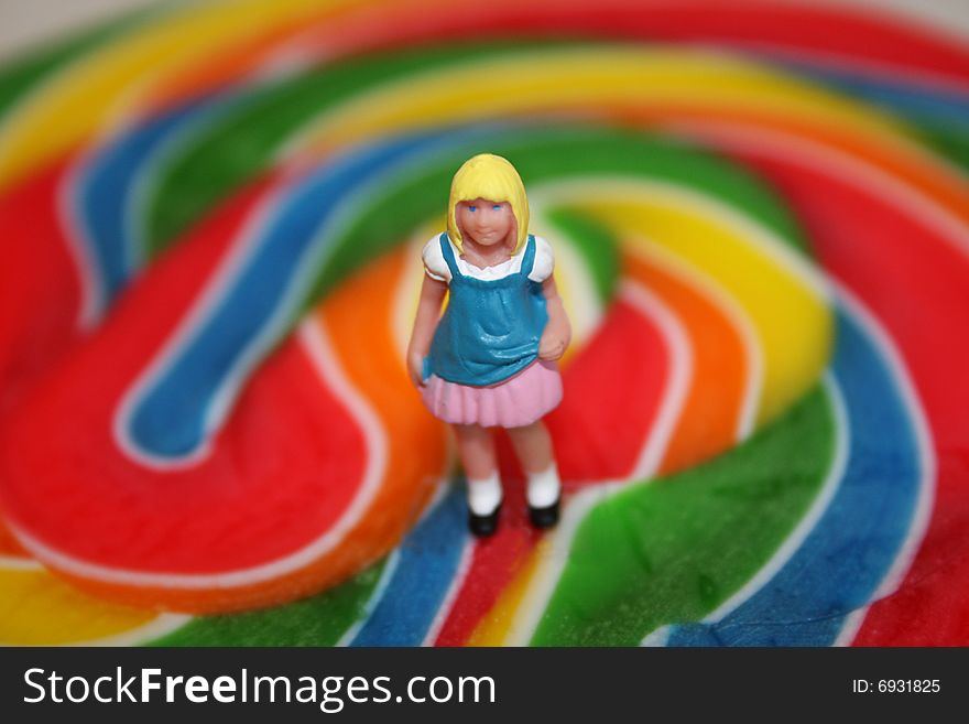 A miniature girl figure stands on top of a giant sucker or lollipop. A miniature girl figure stands on top of a giant sucker or lollipop.