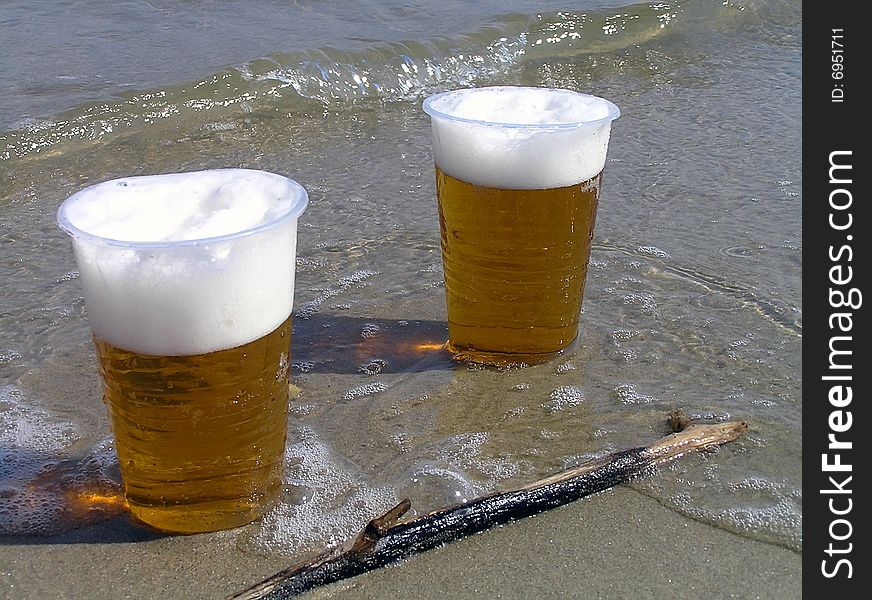 Two disposable plastic glasses with beer on sand at the sea. Two disposable plastic glasses with beer on sand at the sea.