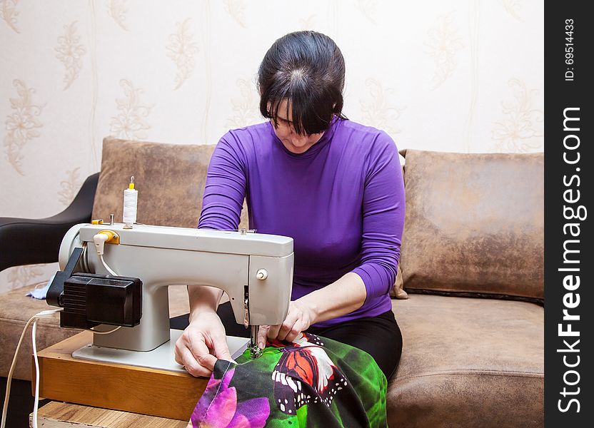 Young brunette woman in blue blouse sewing on the sewing machine. Young brunette woman in blue blouse sewing on the sewing machine