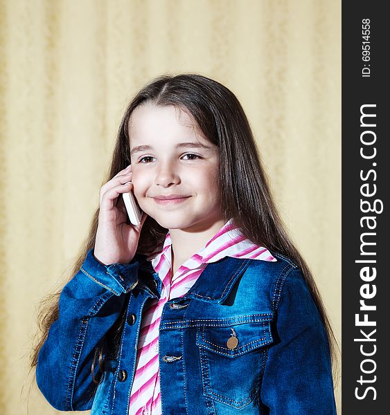 Smiling girl with long hair in a blue denim jacket talking on a phone. Smiling girl with long hair in a blue denim jacket talking on a phone