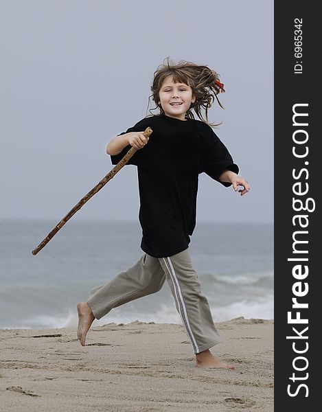 A young girl running on the beach carrying a stick