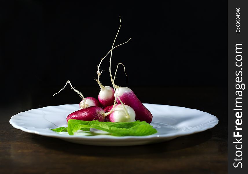 Fresh radishes in white plate on old wooden table