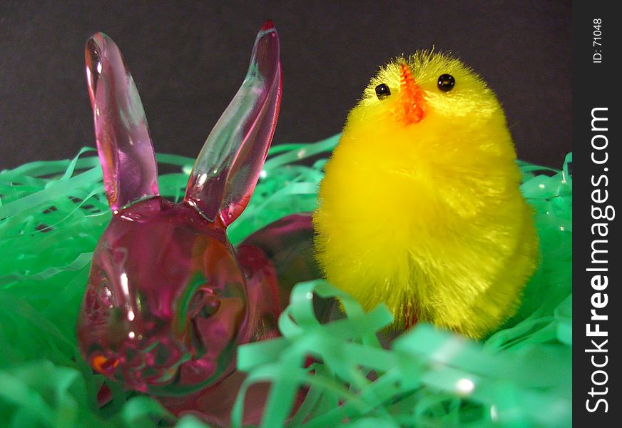 A rose glass bunny with a young chick in a nest of grass. A rose glass bunny with a young chick in a nest of grass.