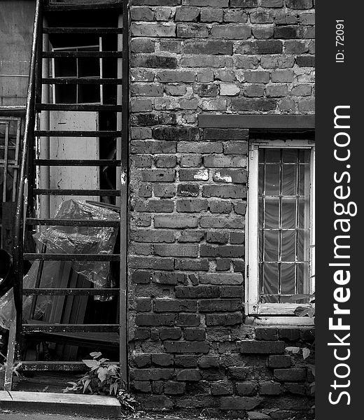 Black and white view of an old iron staircase and window in a brick wall. Black and white view of an old iron staircase and window in a brick wall.