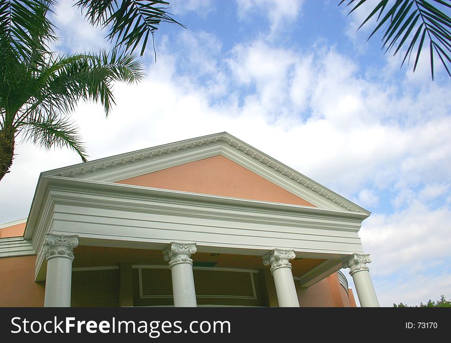 Four ornate columns on terra cotta building,against a cloudy blue sky and tropical foliage. Four ornate columns on terra cotta building,against a cloudy blue sky and tropical foliage