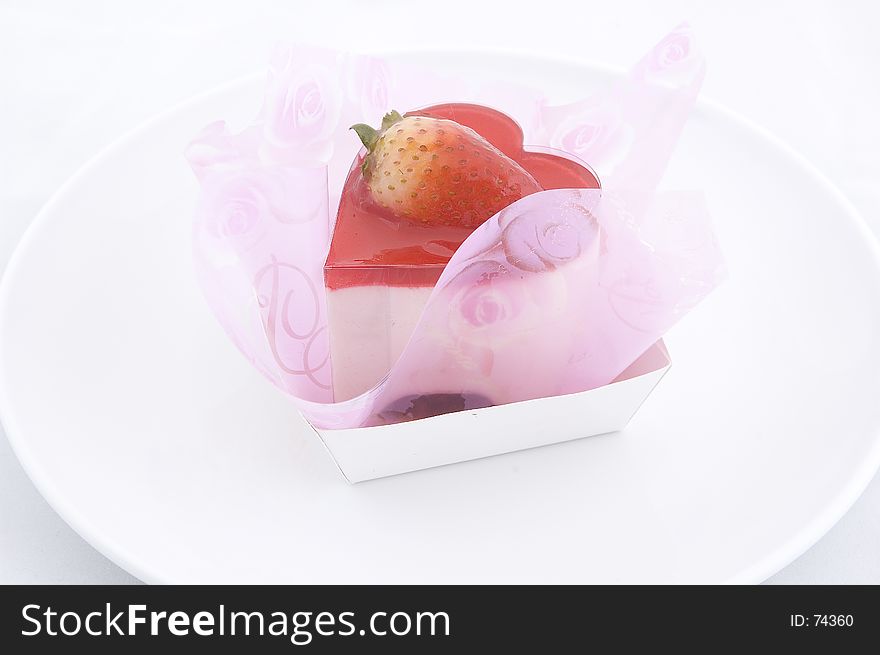 A heart-shaped cake wrapped in pink tissue on a white plate. A heart-shaped cake wrapped in pink tissue on a white plate