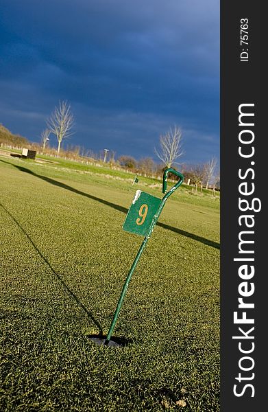 The 9th hole on a putting green with a dramatic sky in the background