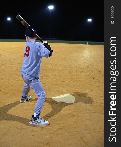 Young boy waiting for a Baseball pitch. It is night. There are stadium lights in the distance. Young boy waiting for a Baseball pitch. It is night. There are stadium lights in the distance.