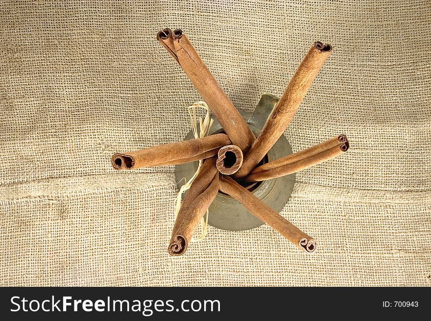 Cinnamon sticks in container on linen background viewed from above