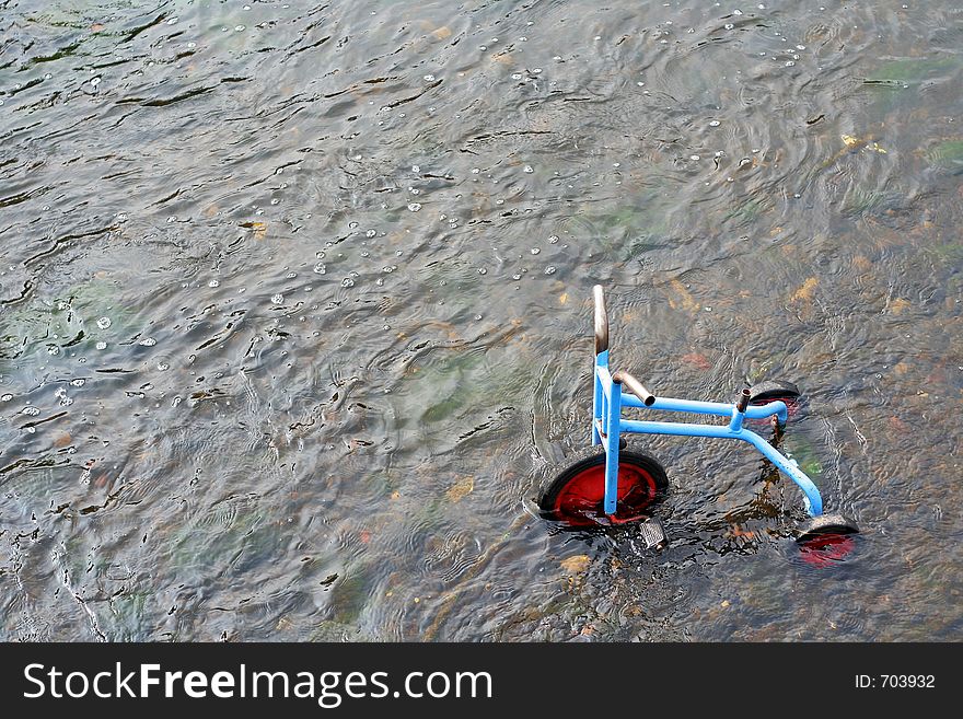 A childs tricycle dumped in a river. A childs tricycle dumped in a river.