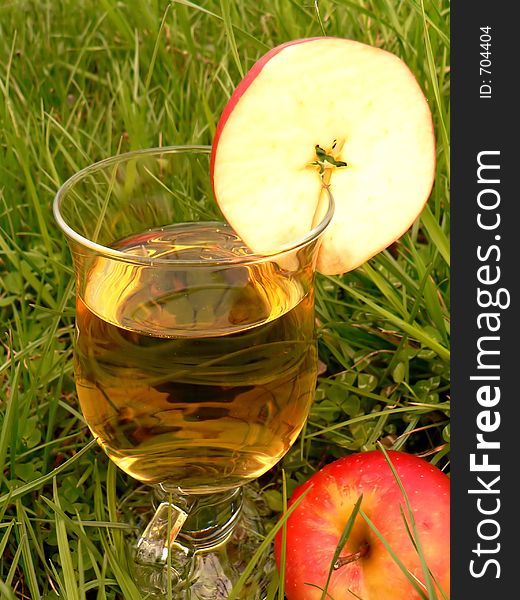 Drink in glass in the grass with an apple slice. Drink in glass in the grass with an apple slice