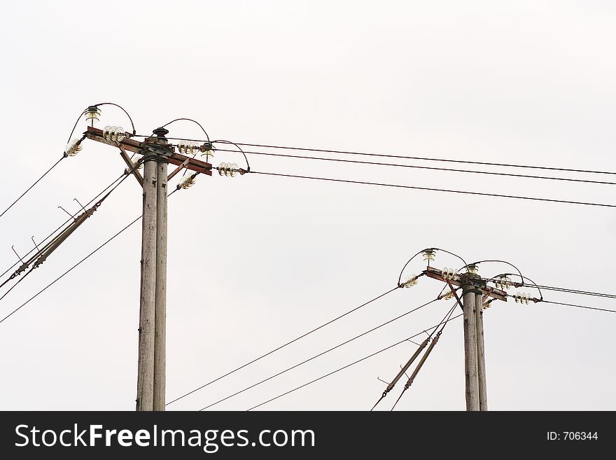 Two poles carrying power lines with an overcast sky behind them. Two poles carrying power lines with an overcast sky behind them.
