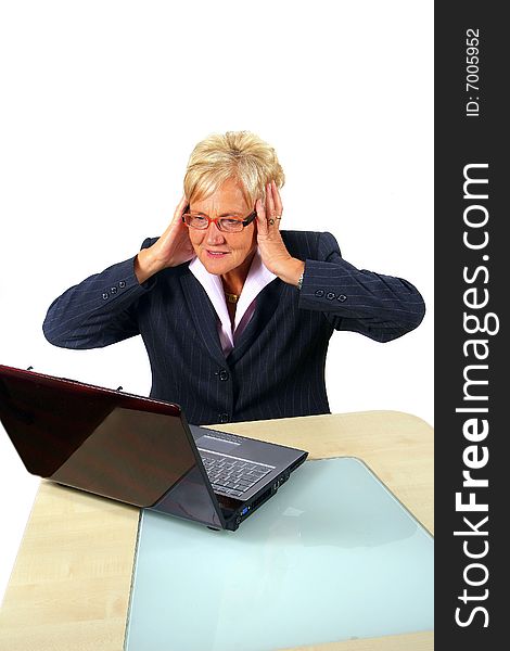 A businesswoman in her sixties in front of a laptop shocked with her hands on her head. Isolated over white. A businesswoman in her sixties in front of a laptop shocked with her hands on her head. Isolated over white.
