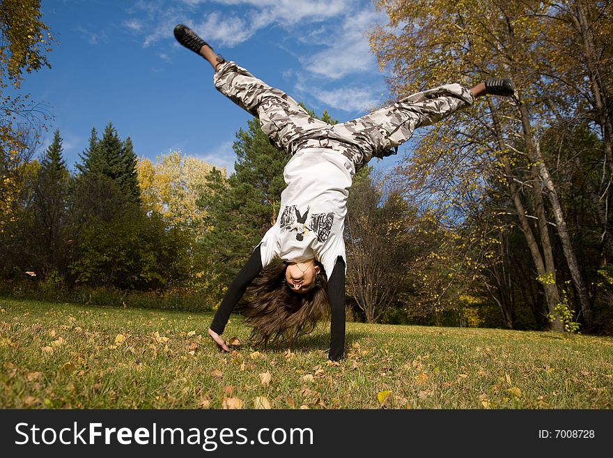 A young woman makes a handstand on grass in front of blue sky