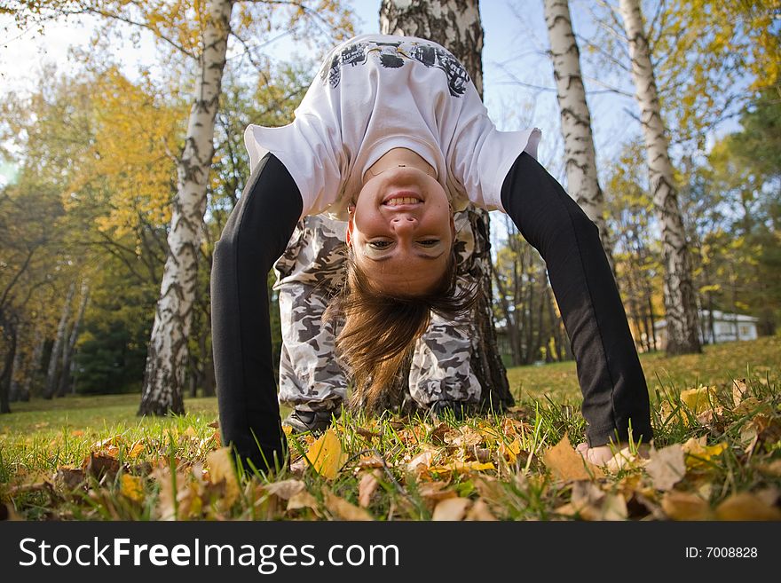 A young woman makes a handstand on grass in front of blue sky