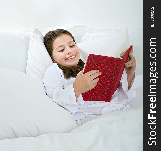 Young girl lying in bed and reading a red book. Young girl lying in bed and reading a red book