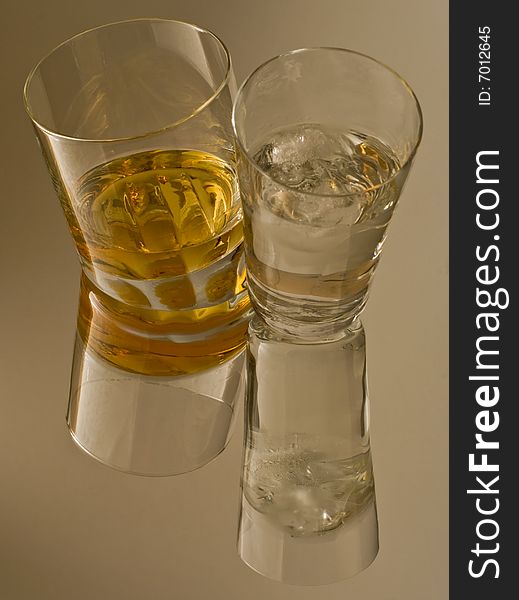 A glass of whiskey and a glass of ice water reflected in the surface. A glass of whiskey and a glass of ice water reflected in the surface.
