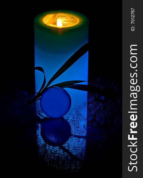 A blue candle and a transparent glass sphere against a black background.