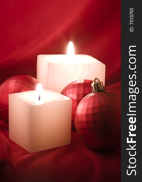 Two cube shaped candles with three baubles over a red silk background. Two cube shaped candles with three baubles over a red silk background.