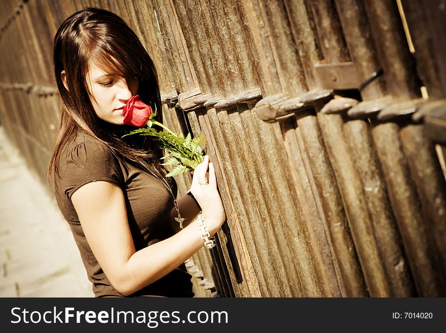 Young woman smelling a red rose over metal fence. Young woman smelling a red rose over metal fence.