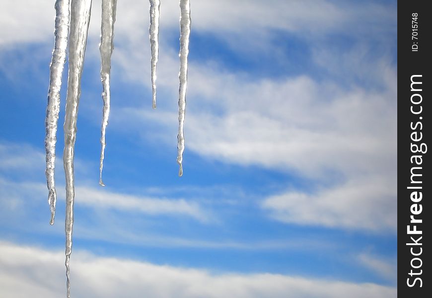 Icicles against a blue sky with clouds.