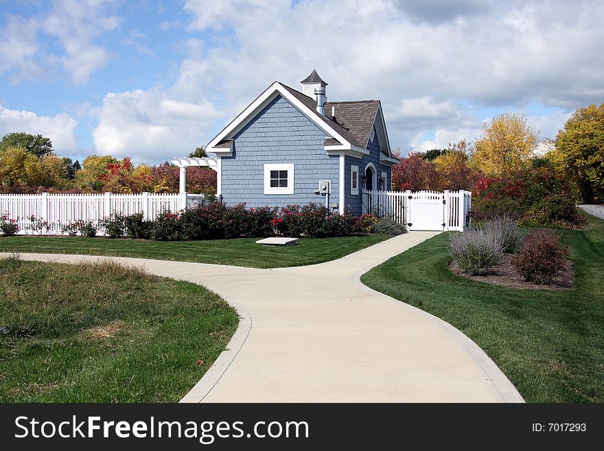 Concrete walkway leading to a blue pool house with white trim