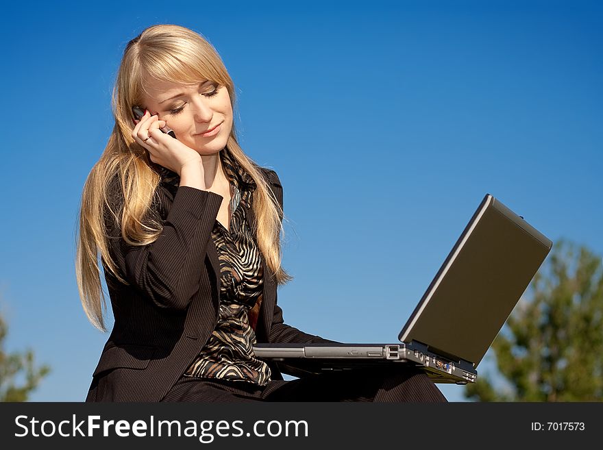 Young blonde business woman working on laptop computer and talking on cell phone. Young blonde business woman working on laptop computer and talking on cell phone