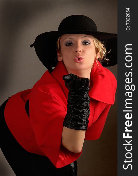 Young woman in red coat, black gloves and black hat sending air kiss