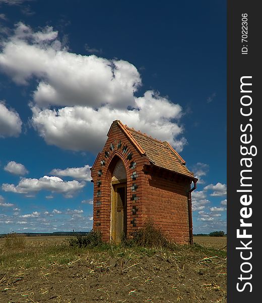 Village chapel in the middle of wide field and blue sky