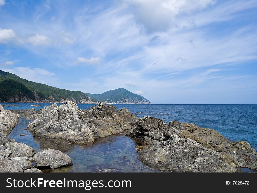 A cloudscape on Japanese sea. On foreground are reefes and stones. A cloudscape on Japanese sea. On foreground are reefes and stones.