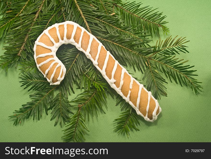 Candy cane cookie with fir branch isolated on green paper. Candy cane cookie with fir branch isolated on green paper