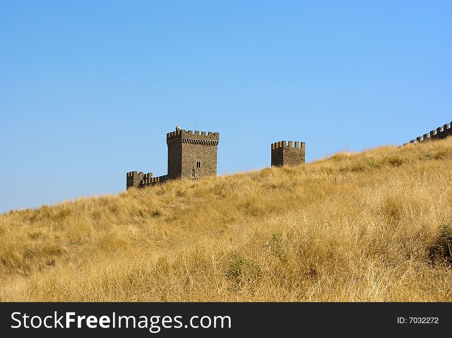 Old medieval stronghold uprising behind a yellow hill against blue sky background. Old medieval stronghold uprising behind a yellow hill against blue sky background