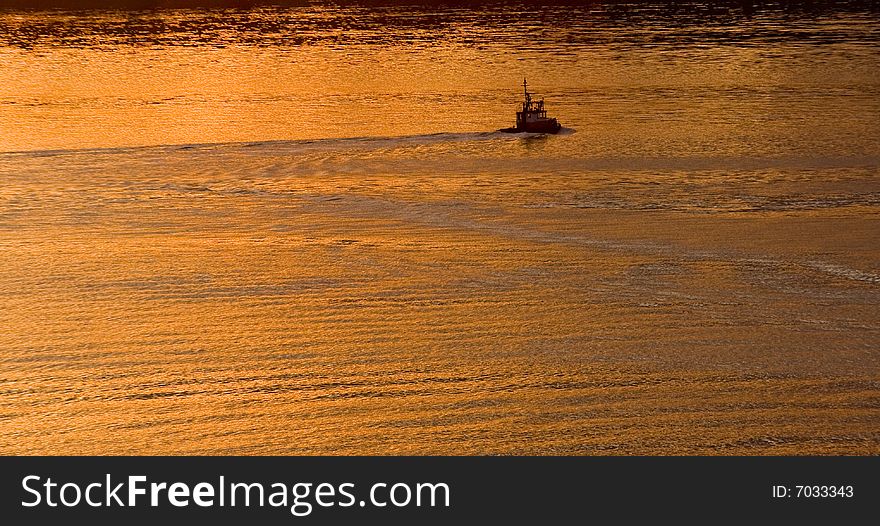 A pilot or tug boat moving through a bay in the golden light of dawn. A pilot or tug boat moving through a bay in the golden light of dawn