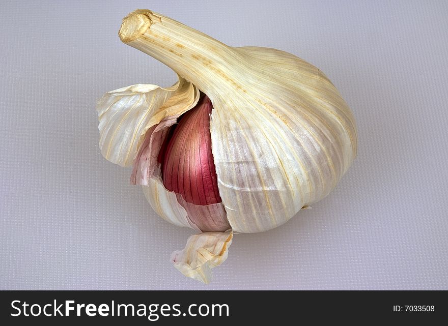 A garlic bulb with one red clove showing. A garlic bulb with one red clove showing