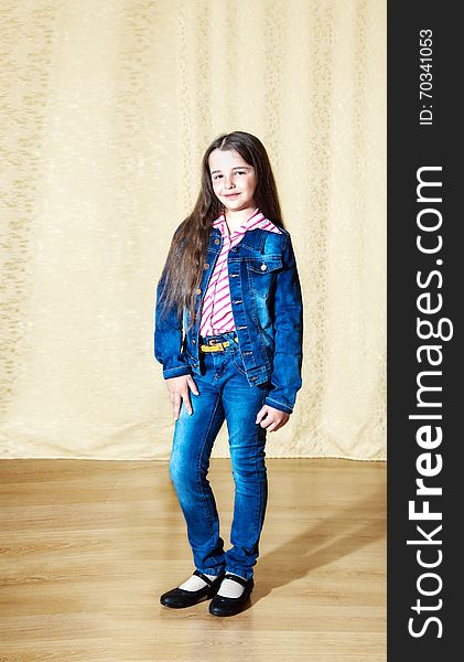 Smiling girl brunette with long hair in a blue denim suit posing while standing in the studio. Smiling girl brunette with long hair in a blue denim suit posing while standing in the studio