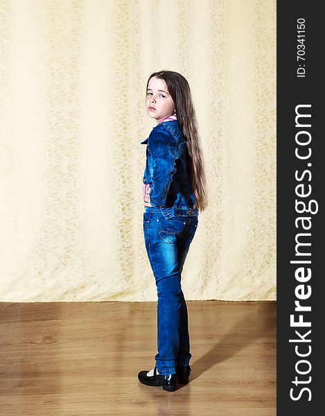 Little girl with long hair in a blue denim suit posing while standing in the studio