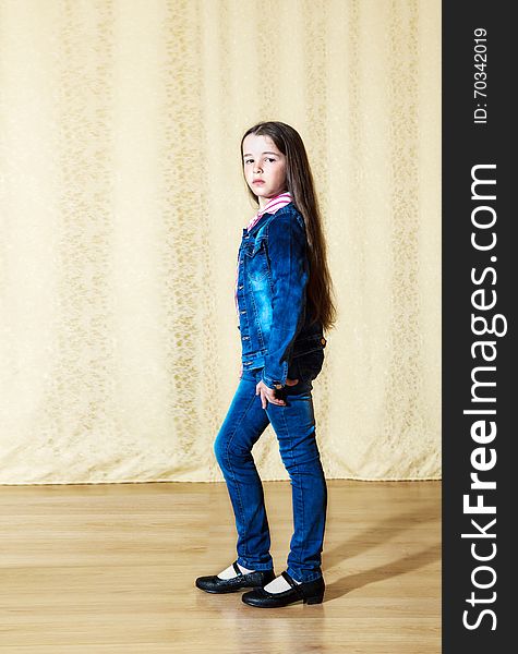 Little girl with long hair in a blue denim suit posing while standing in the studio. Little girl with long hair in a blue denim suit posing while standing in the studio