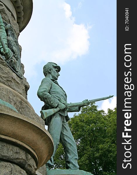 A monument in remembrance of a battle in the Civil War. A bronze statue, that has turned blue green, of a soldier is holding a gun standing on stone monument. Blue skies and green trees are in background. A monument in remembrance of a battle in the Civil War. A bronze statue, that has turned blue green, of a soldier is holding a gun standing on stone monument. Blue skies and green trees are in background.